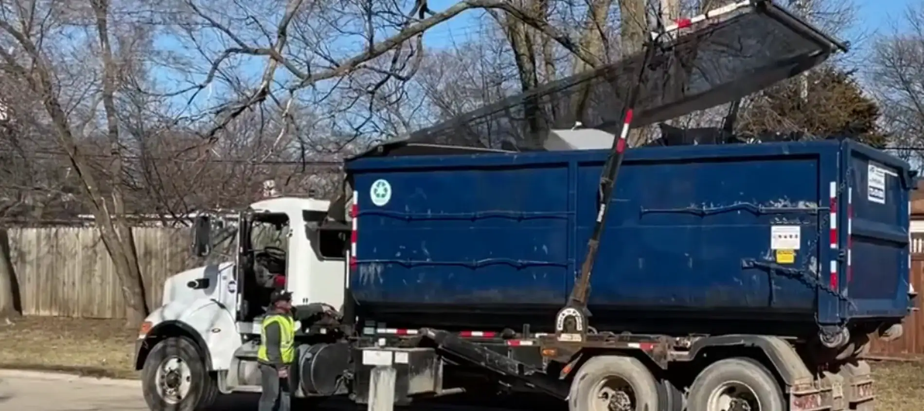A clean navy roll-off dumpster on a residential driveway in Amarillo, TX, beside a pickup truck.