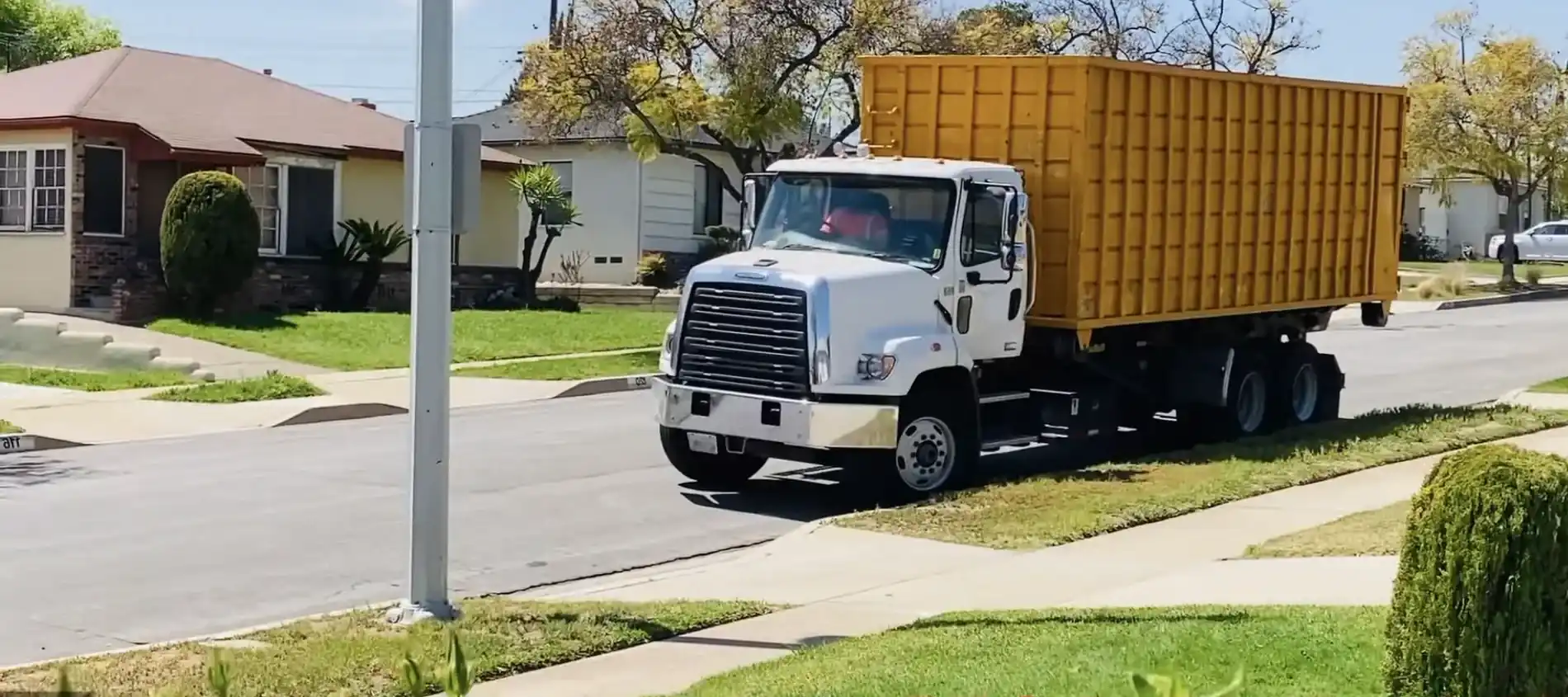 A roll-off truck tipping a large orange dumpster into place.