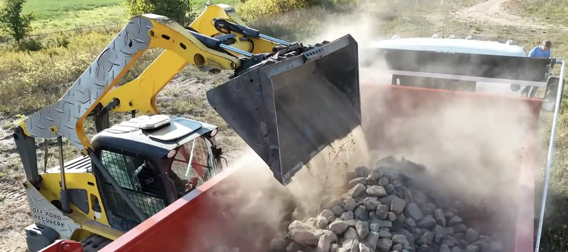 Heavy rock and dirt being loaded into a roll-off dumpster on an Amarillo job site.