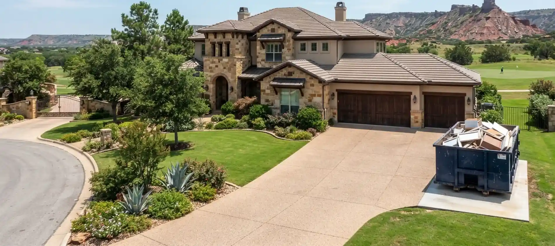 A roll-off dumpster at a gated stone estate in Lake Tanglewood, TX, with canyon bluffs nearby.