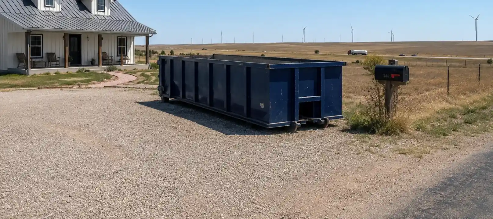A roll-off dumpster by a rural farmhouse near Wildorado, TX, with wind turbines on the horizon.