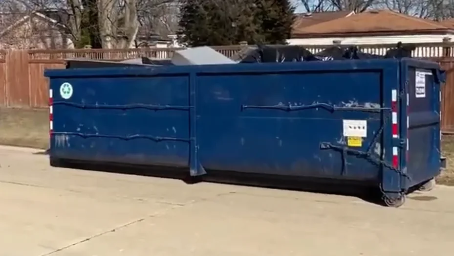 A roll-off dumpster sitting on a driveway, ready for pickup at the end of a rental period
