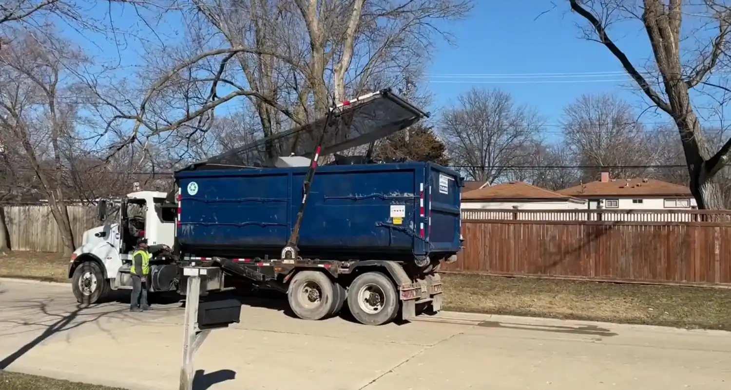 A worker checking a roll-off dumpster's load before pickup