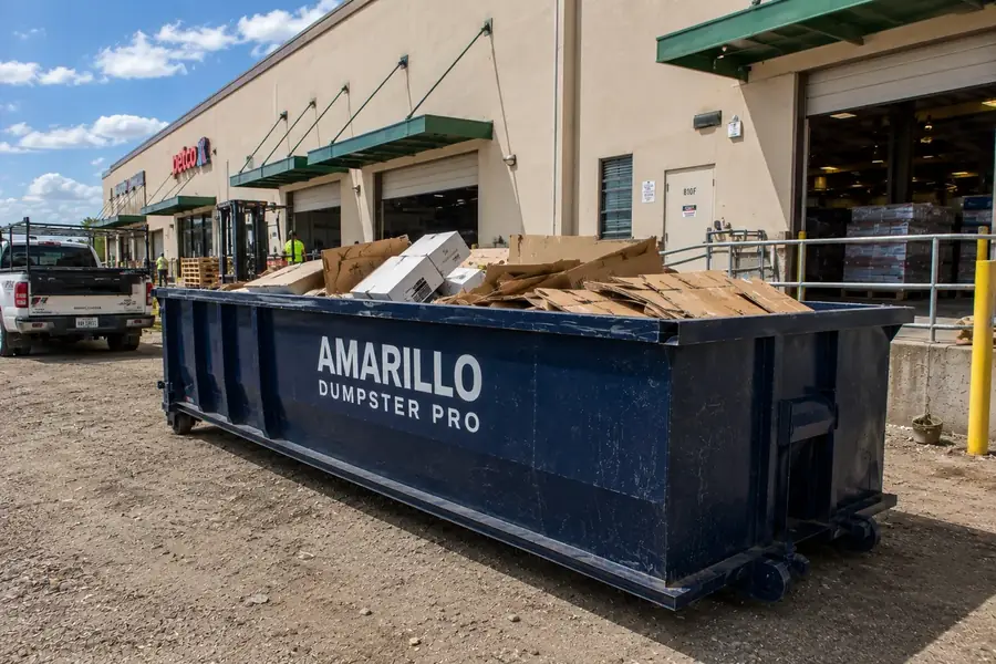 A roll-off dumpster loaded with cardboard and packaging debris outside a retail loading dock.
