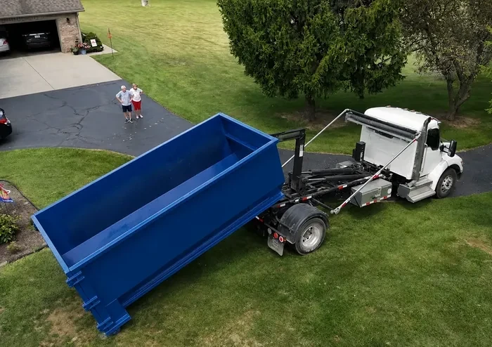 Aerial view of a roll-off dumpster being placed on a residential lawn by a roll-off truck