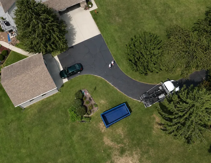 Aerial view of a dumpster on the grass beside a garden bed, truck parked in the driveway.