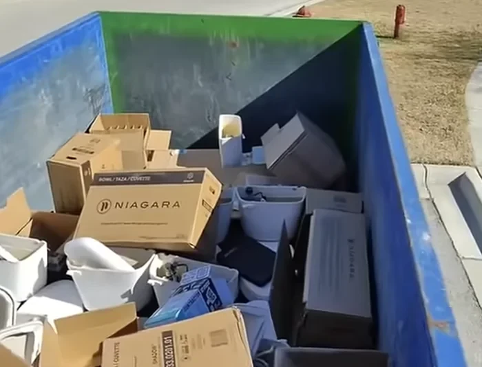 Dumpster loaded with new bathroom fixtures and packaging, including toilets and vanity boxes.