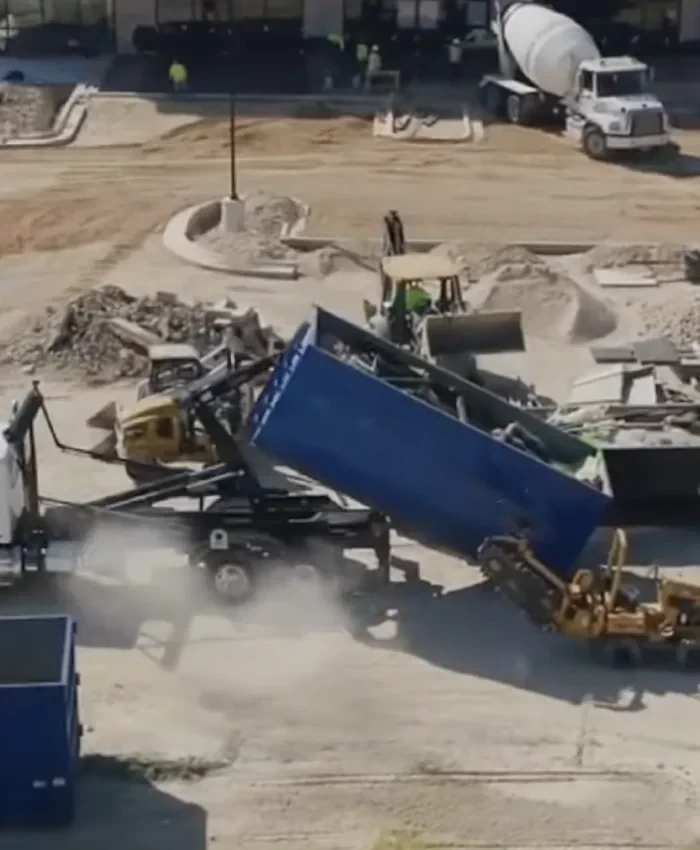 Aerial view of a dumpster on a commercial build-out, with a mixer truck and excavator nearby.
