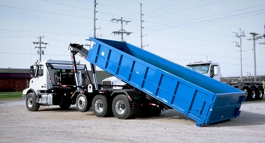 An empty roll-off dumpster with its mesh tarp cover on a delivery truck