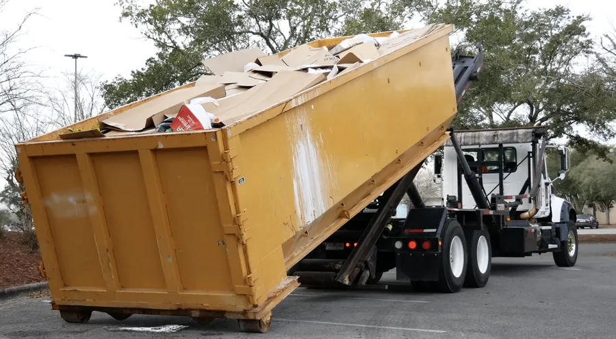 A roll-off dumpster loaded with cardboard at a commercial parking lot