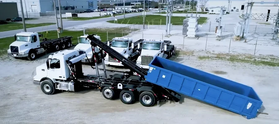 Wide aerial view of four roll-off trucks and an empty dumpster in the equipment yard