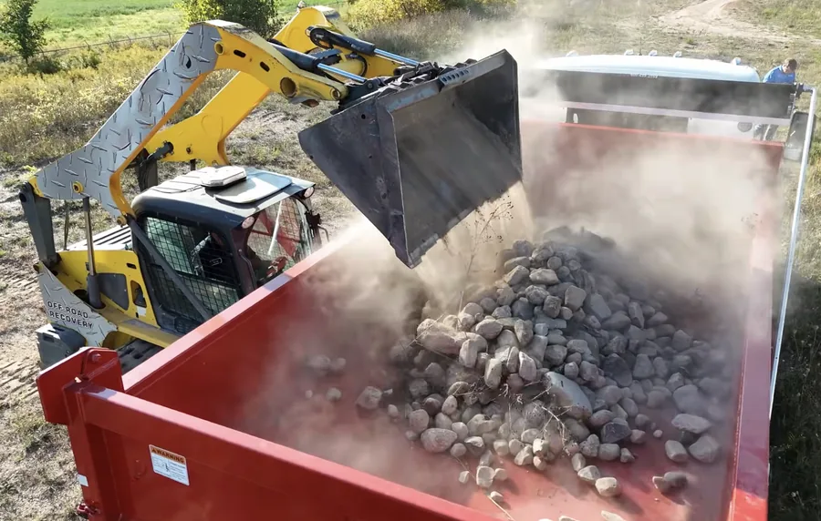 Heavy rock and debris being loaded into a roll-off dumpster