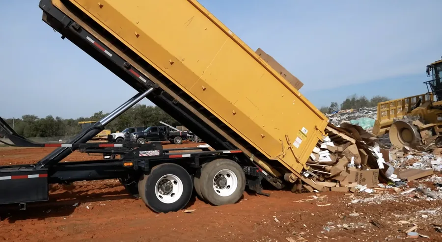 Close-up of a roll-off dumpster tipping cardboard and debris at the landfill
