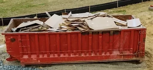 A roll-off dumpster loaded with drywall and trim debris from a remodel