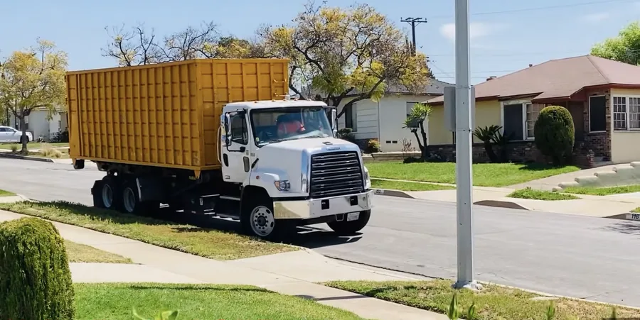 A yellow roll-off dumpster staged on a residential street during a driveway delivery
